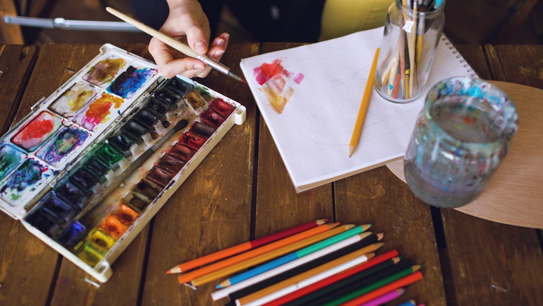 Artist painting with watercolors and colored pencils on wooden table.