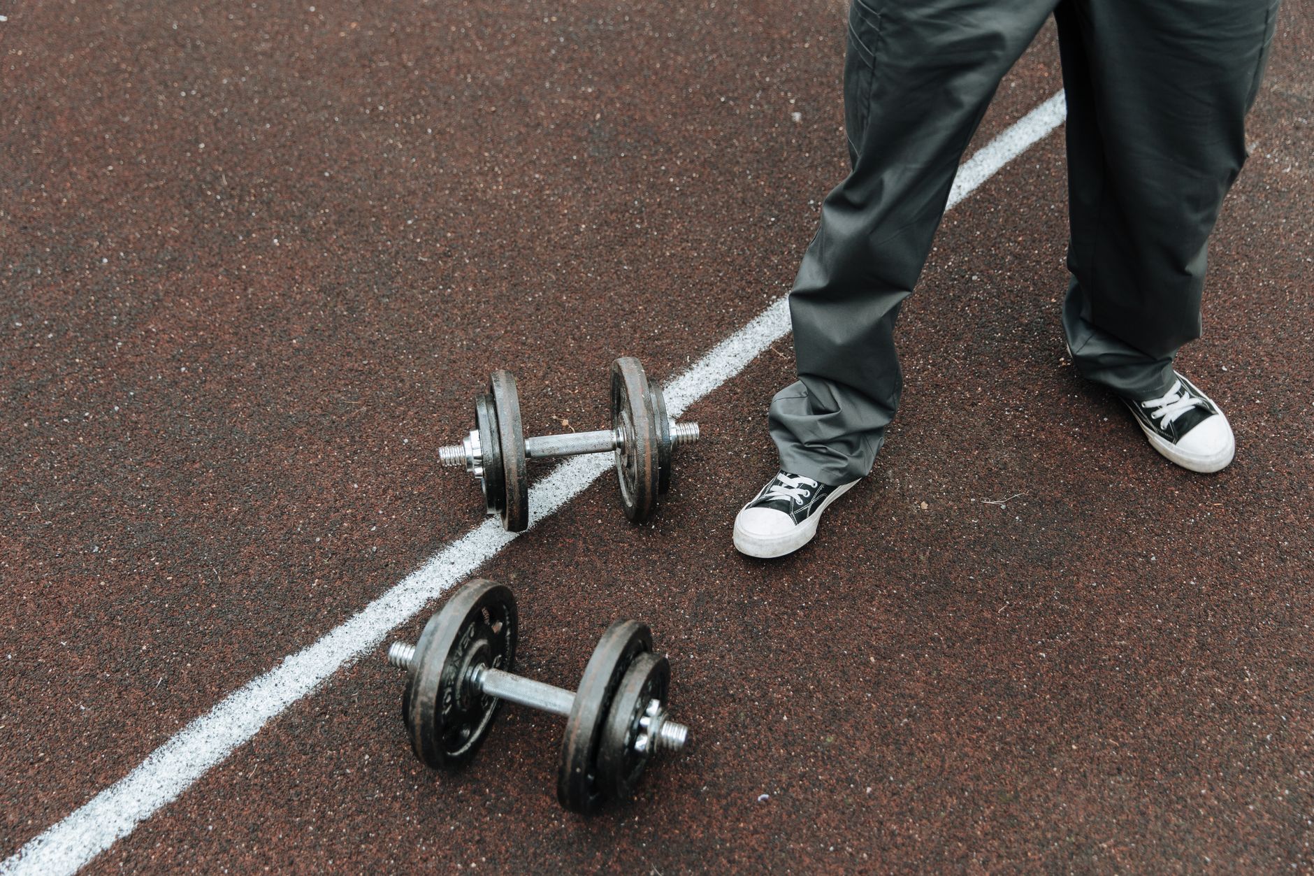 Dumbbells on an outdoor sports track with a person in casual wear.