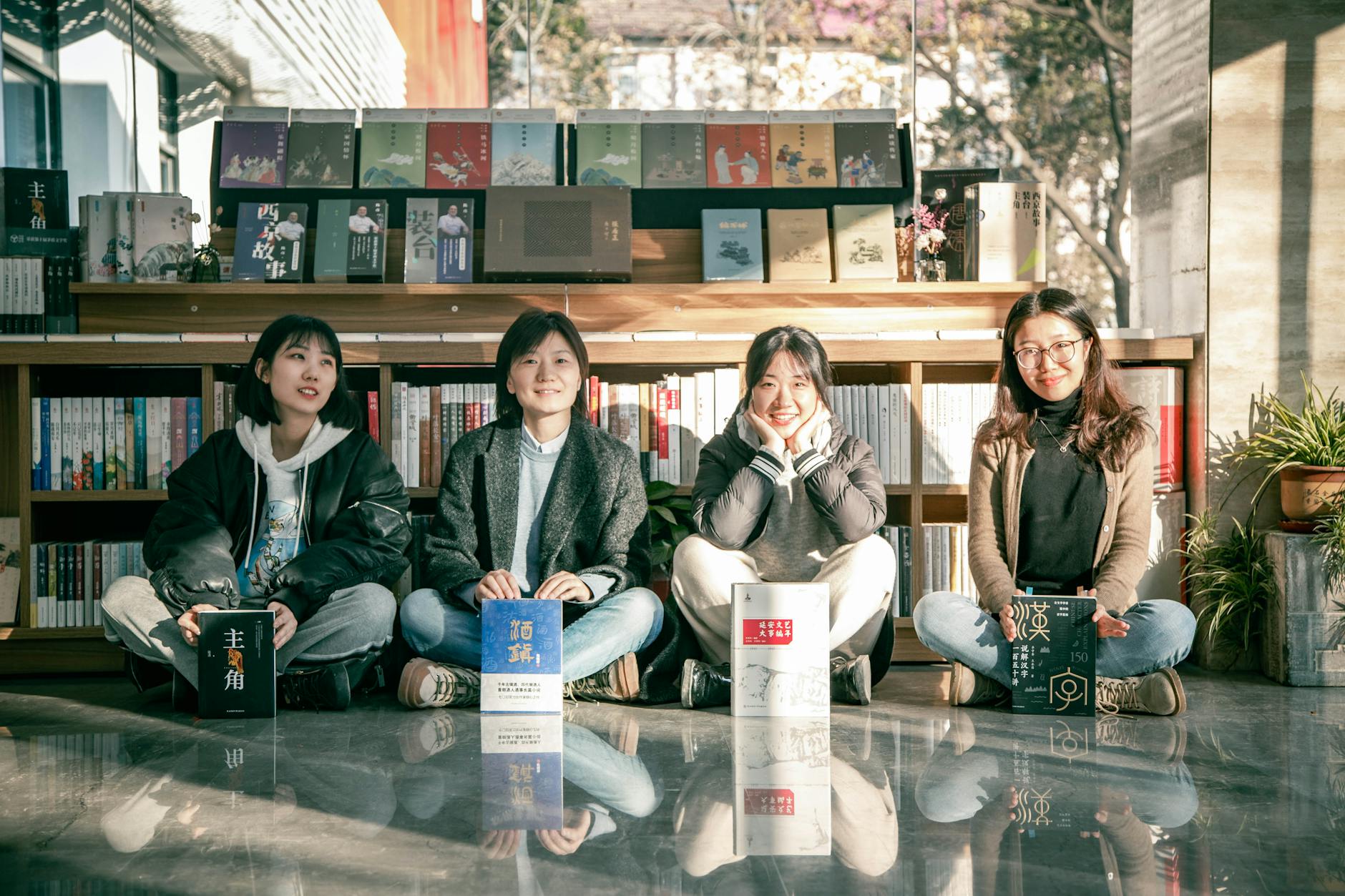 Four young women sitting in a sunny bookstore, enjoying books and friendship.
