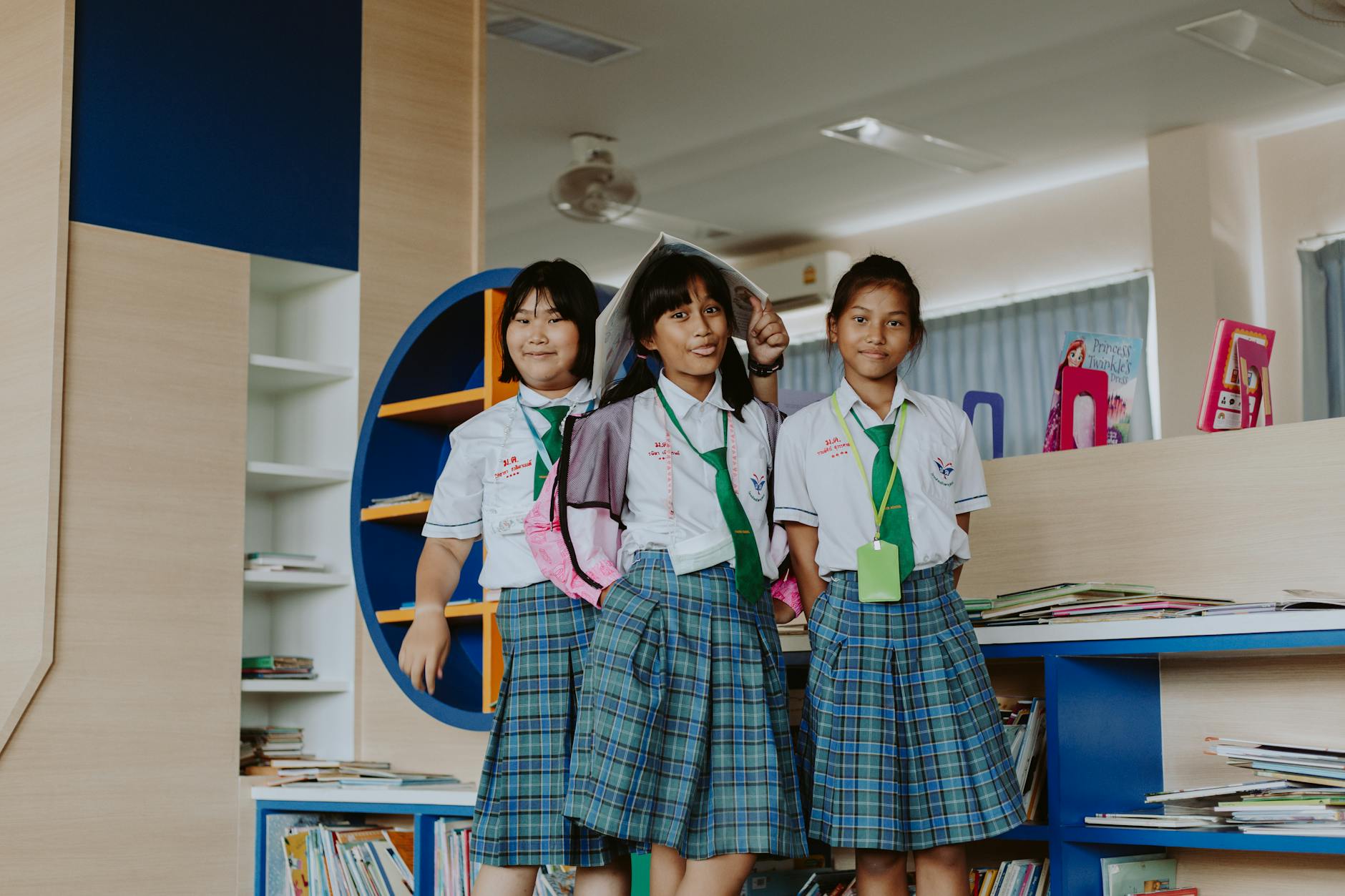 Three schoolgirls in uniform smiling happily while posing inside a library.