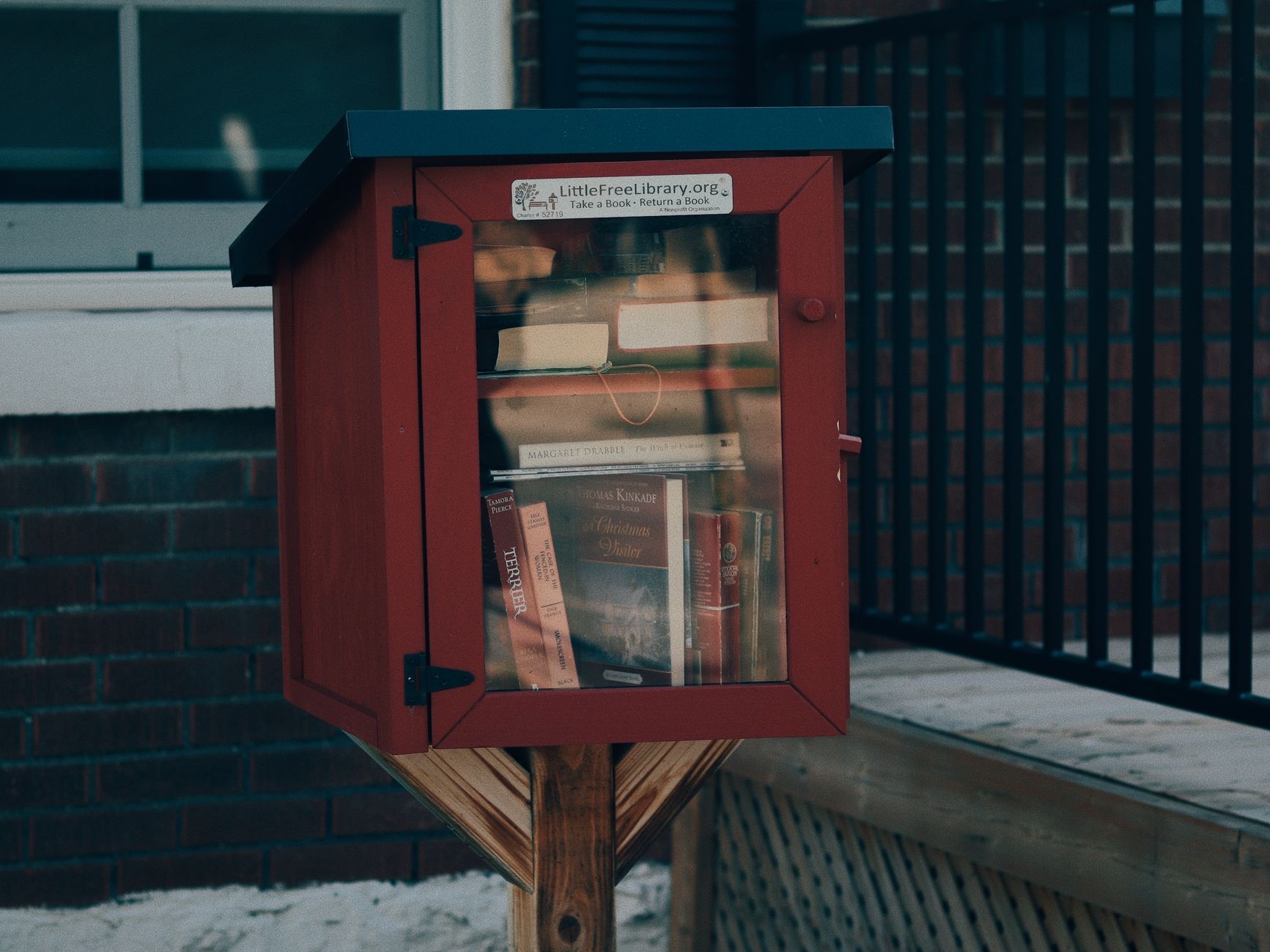 Small red box filled with books, part of a Little Free Library on a city street.