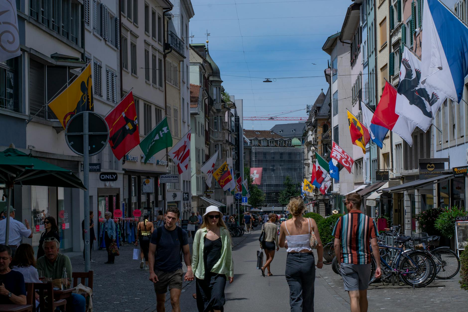 A bustling Zürich city street adorned with colorful flags and pedestrians enjoying a sunny day.