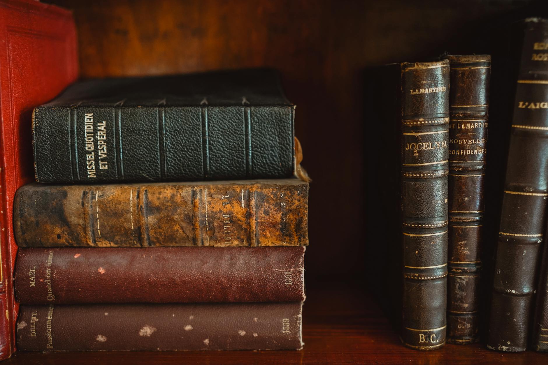 A collection of antique leather-bound books on a wooden shelf in a library.