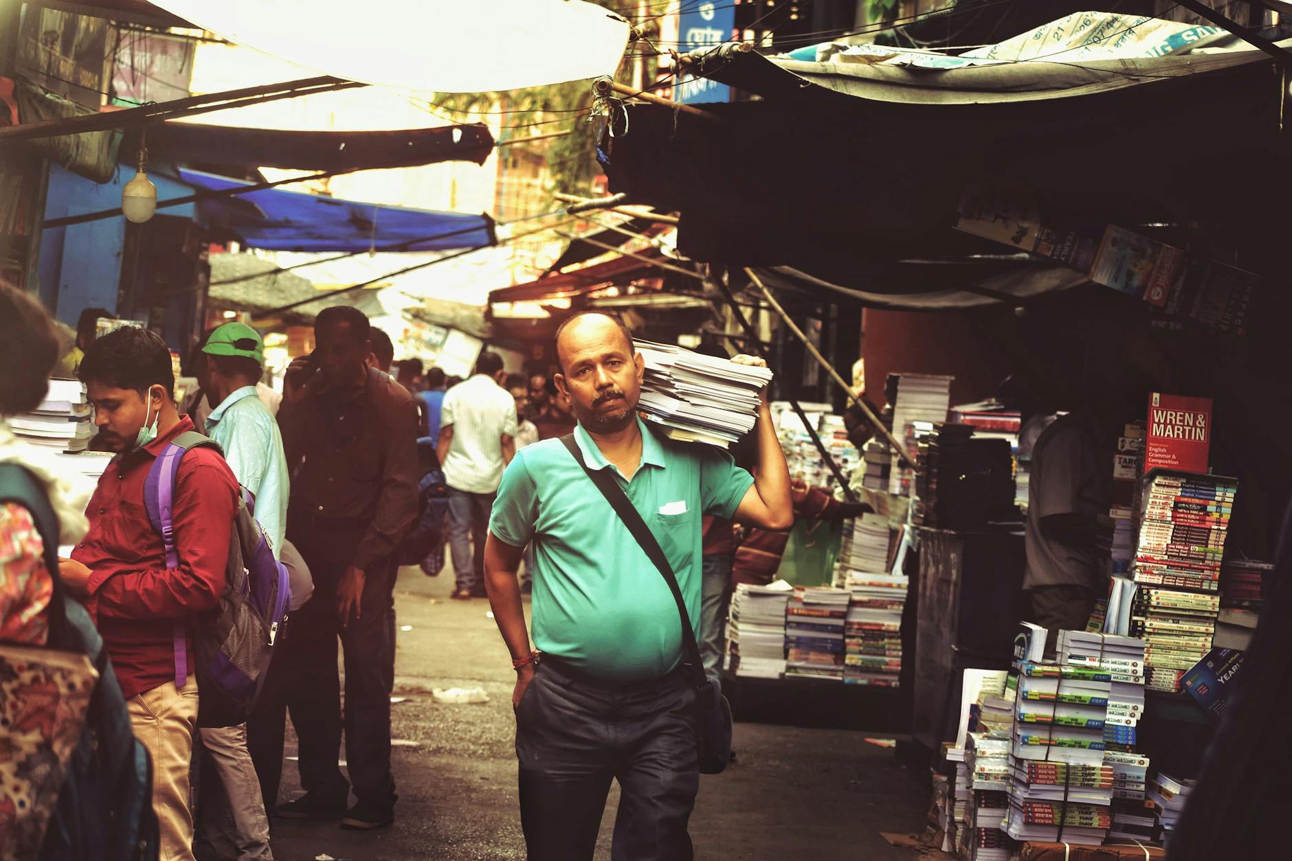 Market street scene with vendors and stacks of books, bustling with activity and people shopping.