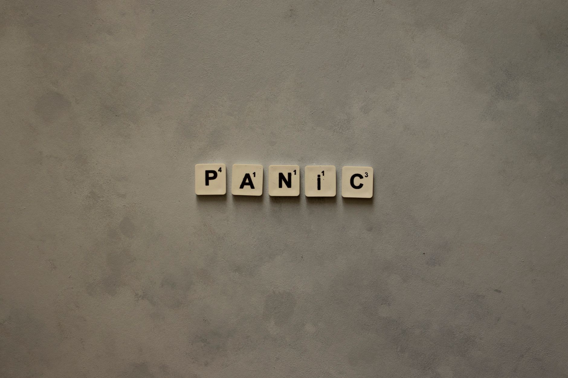 Scrabble tiles forming the word 'Panic' on a simple neutral background, symbolizing anxiety.