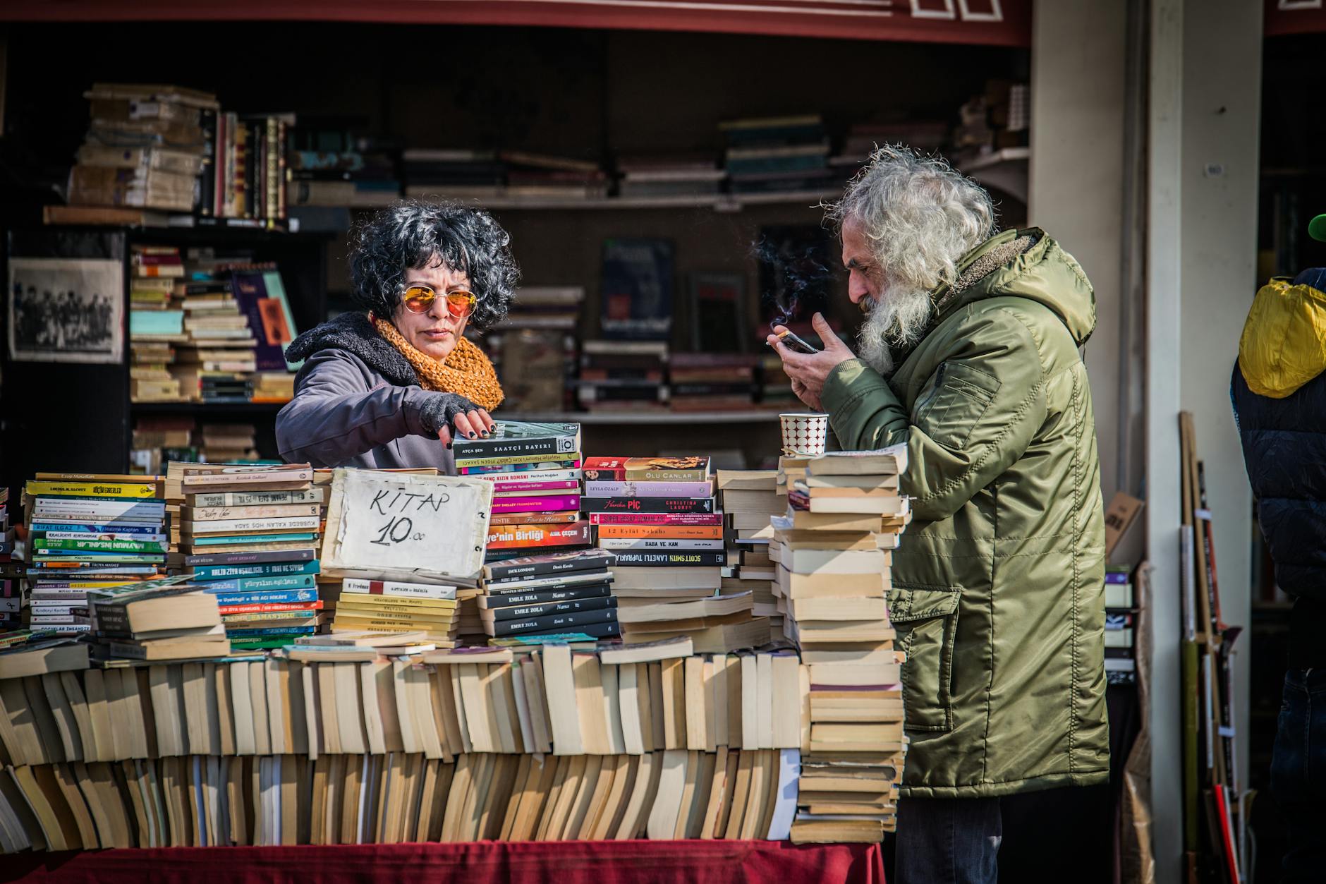 A lively street book market scene in Istanbul with people browsing books and a vendor smoking.