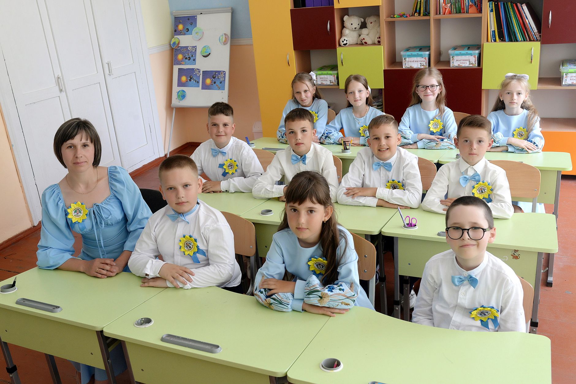 A classroom of children in blue and white uniforms seated with their teacher.