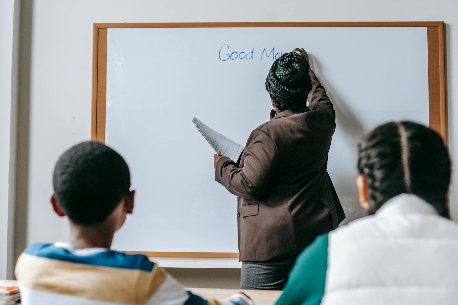 Back view unrecognizable African American female teacher wearing formal clothes writing on whiteboard for multiethnic elementary classmates