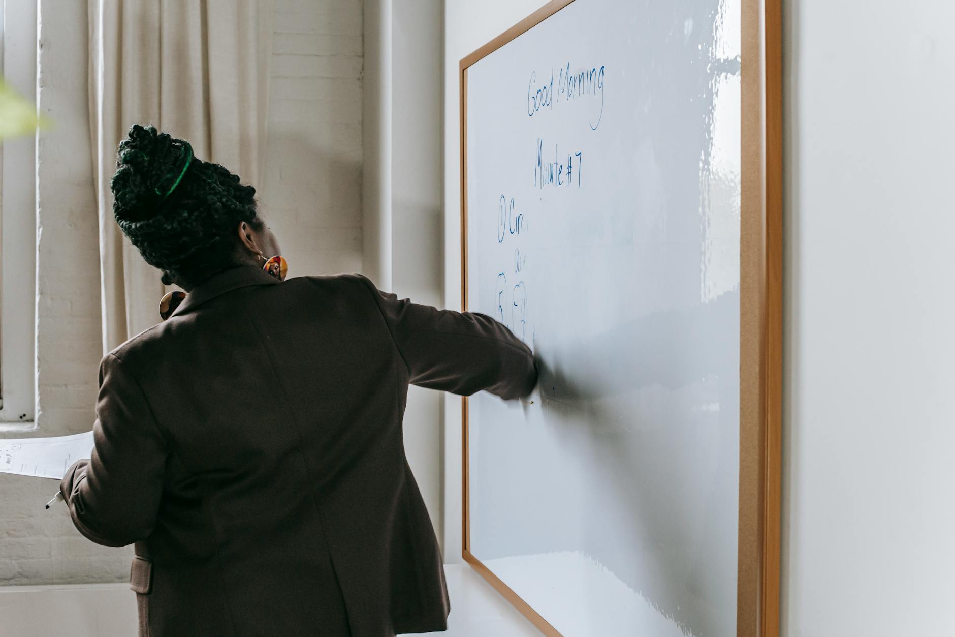 Back view unrecognizable African American female teacher writing on whiteboard and explaining new material during lesson in classroom