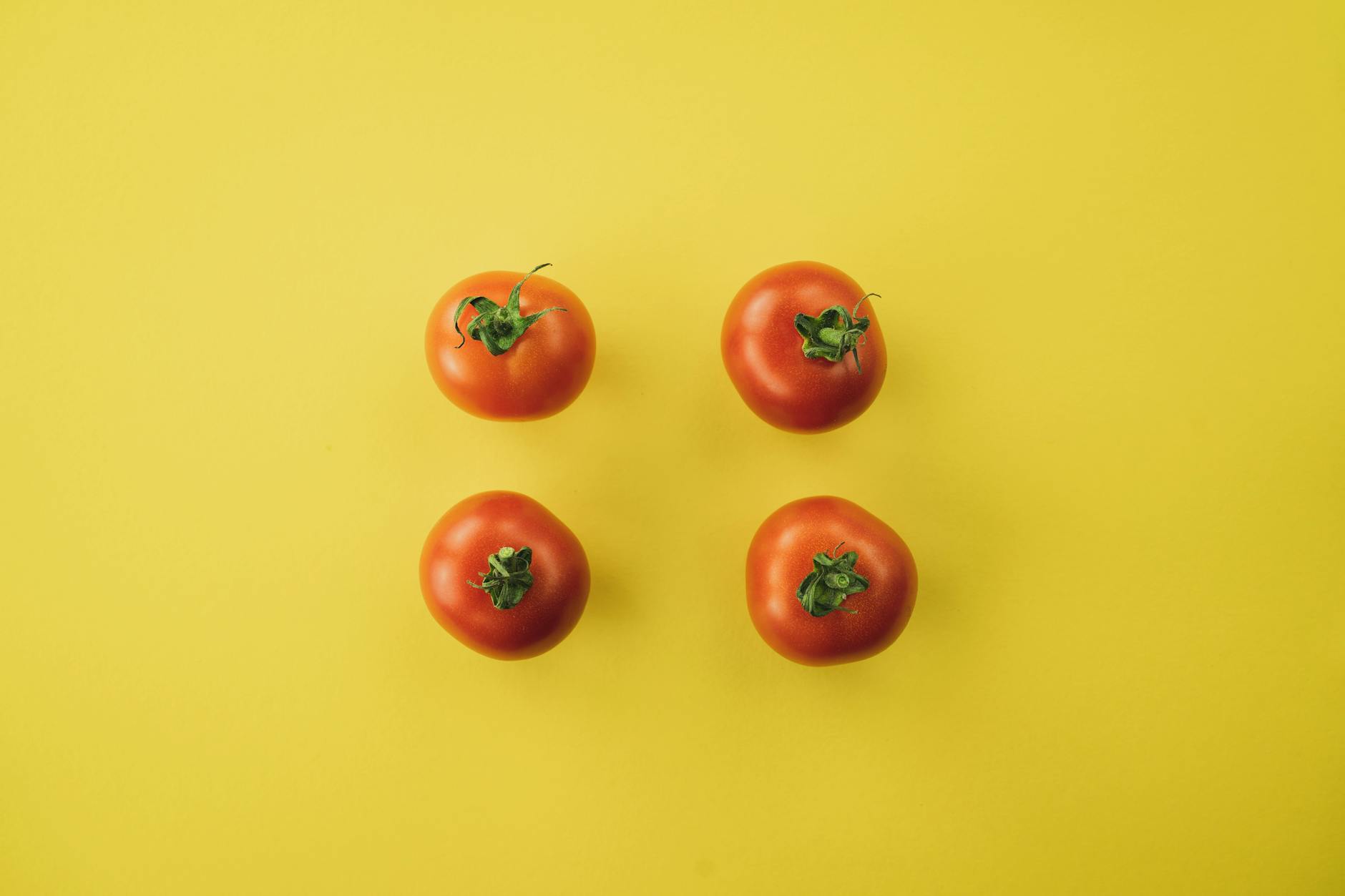 Minimalist arrangement of fresh red tomatoes on a vibrant yellow background, creating a bold contrast.