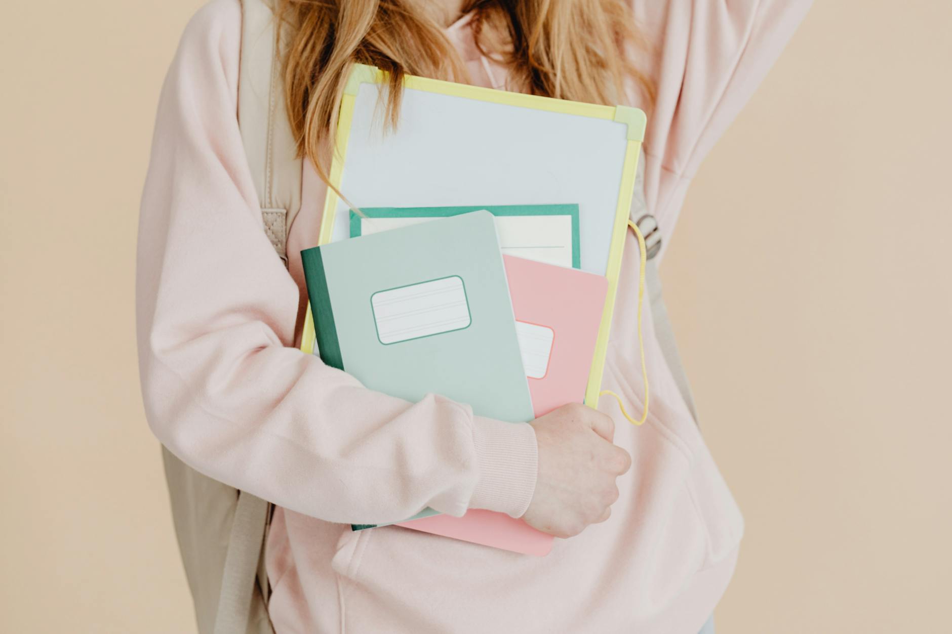Young student in pink hoodie holding colorful notebooks, ready for school.