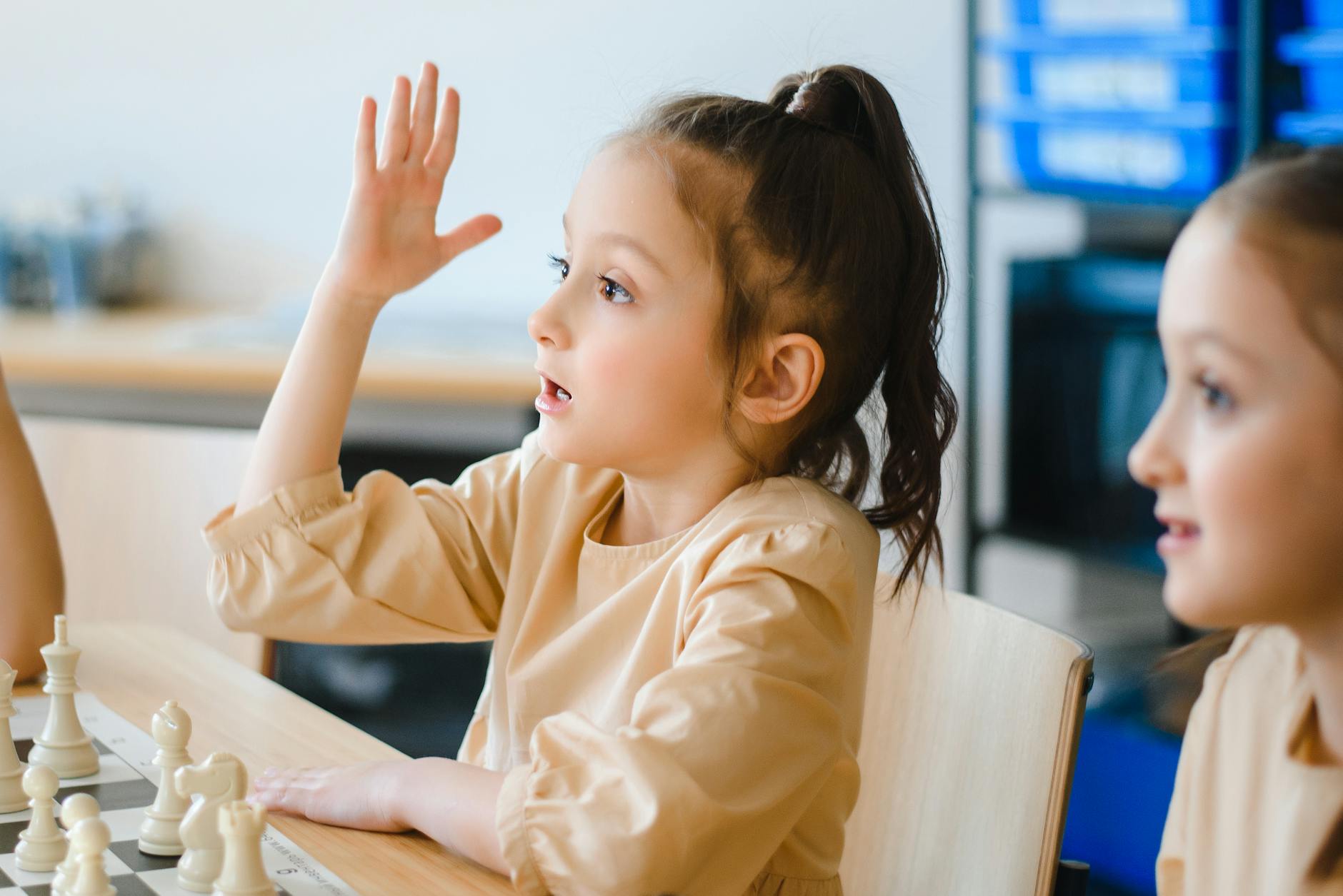 A young girl raising her hand while participating in a classroom chess activity.